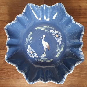 Puede incluir: Un cuenco de cerámica azul con un diseño de cigüeña blanca y flores. El cuenco tiene un borde festoneado y es perfecto para servir fruta o aperitivos.