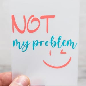 Könnte beinhalten: Eine weiße rechteckige Karte mit dem Text NOT in Korallenrot, gefolgt von den Wörtern my problem in einer türkisfarbenen Schreibschrift und einer korallenroten zwinkernden Smiley-Grafik unter dem Text auf der rechten Seite.