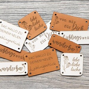 Könnte beinhalten: Eine Sammlung von rechteckigen und quadratischen Kunstleder-Etiketten in Hellbraun und Weiß mit lasergravierten Texten wie "lebe liebe lache", "von mir für Dich", "wunderbar" und "SAG HALLO ZU DEINEM NEUEN Lieblingsstück."