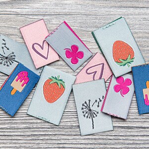 May include: A collection of colourful fabric patches with various embroidered designs, including hearts, strawberries, clovers, dandelions, and ice cream cones.