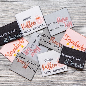 May include: A collection of eight colorful fabric labels with German text. The labels feature various sayings, including "Ohne Kaffee geht nichts!" and "Schreib's auf, ist besser!"  The labels are perfect for adding a touch of personality to handmade items.