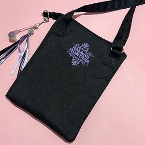 May include: Black canvas shoulder bag with a purple embroidered logo that says "Hannah Montana". The bag has a silver chain with a crystal charm attached.
