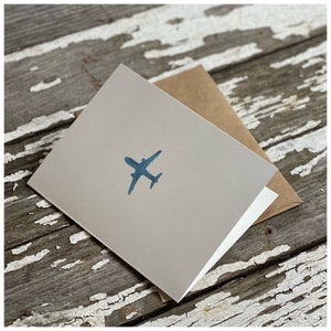 May include: A blank greeting card with a blue airplane silhouette printed on the front. The card is folded in half and has a brown envelope.