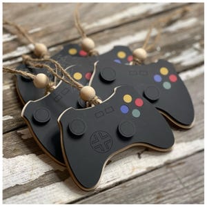 May include: Five black wooden game controller ornaments with colorful buttons. Each ornament has a brown twine loop for hanging.