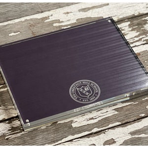 May include: A clear acrylic frame with a dark purple background and a silver embossed seal that reads "The Chestnut Hill School Est. 1869".