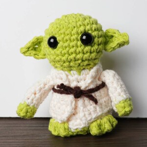 Pu&ograve; includere: Bambola all'uncinetto fatta a mano che assomiglia a un personaggio di un popolare franchise di fantascienza. La bambola ha grandi occhi neri, pelle verde e grandi orecchie. Indossa una veste color crema con cintura marrone e piedi verdi.