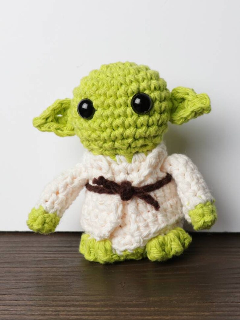Pu&ograve; includere: Bambola all'uncinetto fatta a mano che assomiglia a un personaggio di un popolare franchise di fantascienza. La bambola ha grandi occhi neri, pelle verde e grandi orecchie. Indossa una veste color crema con cintura marrone e piedi verdi.