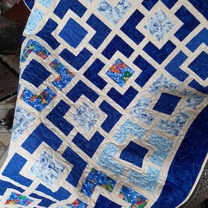 May include: A blue and white quilt with a geometric pattern. The quilt is made of different fabrics with various designs, including fish and seashells.