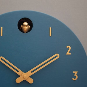May include: A blue cuckoo clock with gold hands and Roman numeral markings. The clock face has a small opening at the top with a gold bird figurine inside.