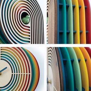 May include: A colorful wooden clock with a rainbow design. The clock face is white with black hands and a small bird cutout in the top right corner.