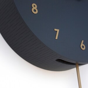 May include: Close-up of a dark blue clock face with gold numbers 5, 6, 7, and 8. The clock has a pendulum.