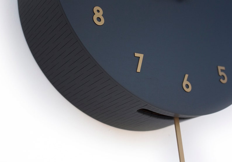 May include: Close-up of a dark blue clock face with gold numbers 5, 6, 7, and 8. The clock has a pendulum.