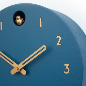 May include: A blue round clock with gold hands and gold numbers. The clock has a small bird that pops out of the top.