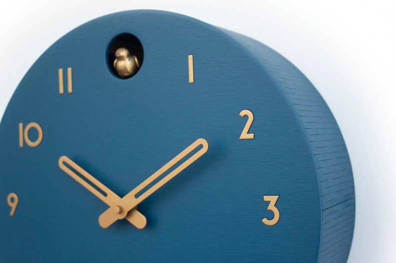 May include: A blue round clock with gold hands and gold numbers. The clock has a small bird that pops out of the top.