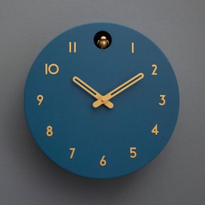 May include: A blue round clock with gold hands and gold numbers. The clock has a cuckoo bird on the top.