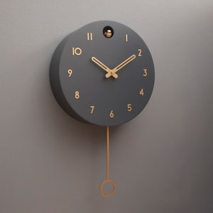 May include: A black pendulum clock with gold-coloured hands and numbers. The clock has a simple design and a minimalist aesthetic.