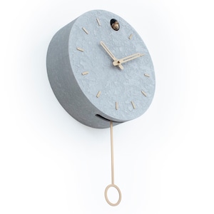 May include: A grey round clock with a pendulum and gold-coloured hands. The clock has a textured surface and a small hole at the top.