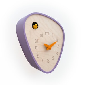 Könnte beinhalten: Eine moderne Kuckucksuhr mit einem hellvioletten Rahmen und einem Zifferblatt aus Naturholz. Die Uhr hat einen orangefarbenen, vogelförmigen Zeiger und einen kleinen gelben Vogel im Inneren. Die Zahlen sind minimalistisch.