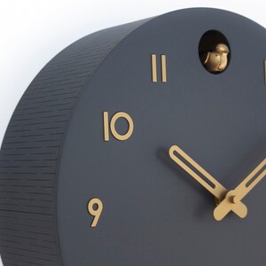 May include: A black and gold cuckoo clock with a bird that pops out of the top. The clock face has Roman numerals and gold hands.