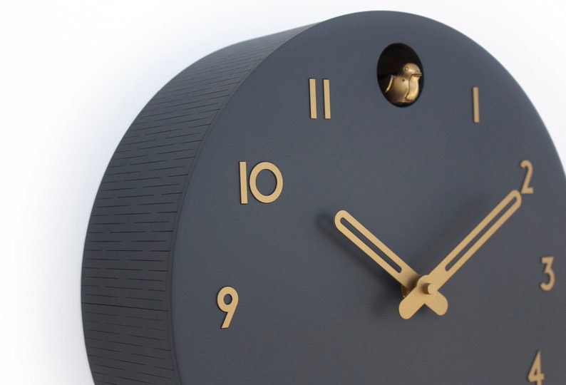 May include: A black and gold cuckoo clock with a bird that pops out of the top. The clock face has Roman numerals and gold hands.
