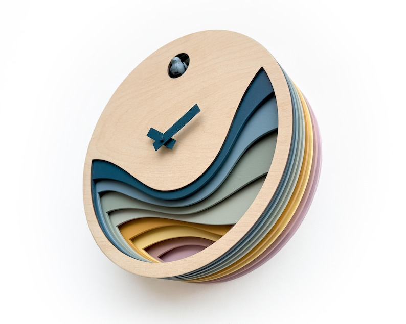 K&ouml;nnte beinhalten: Eine runde Wanduhr aus Holz mit einem geschichteten Design, das blaue, gr&uuml;ne, gelbe und rosa Wellen zeigt. Die Uhr hat einen Kuckuck und ein einfaches schwarzes und blaues Zifferblatt.