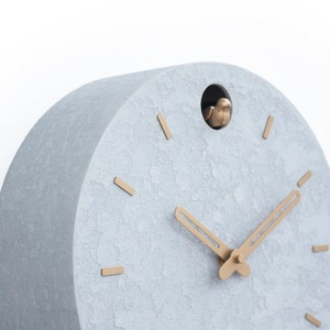 May include: A grey, textured, round cuckoo clock with gold-coloured hands and a small bird that pops out of the hole at the top.