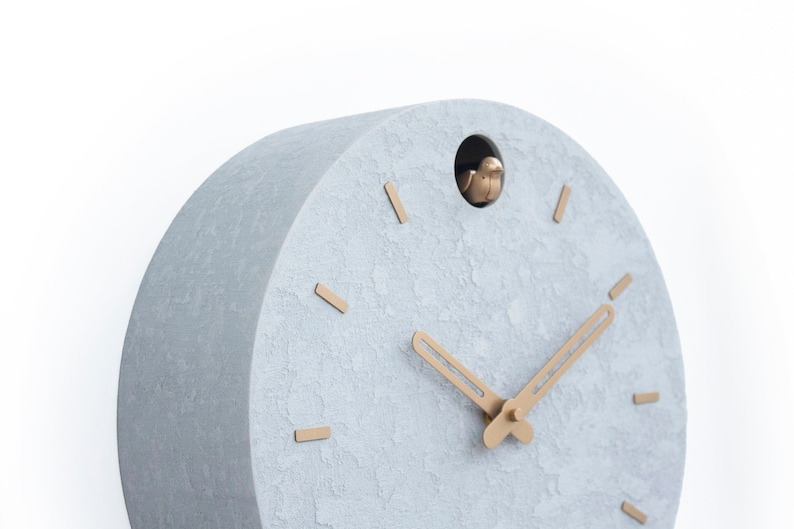May include: A grey, textured, round cuckoo clock with gold-coloured hands and a small bird that pops out of the hole at the top.