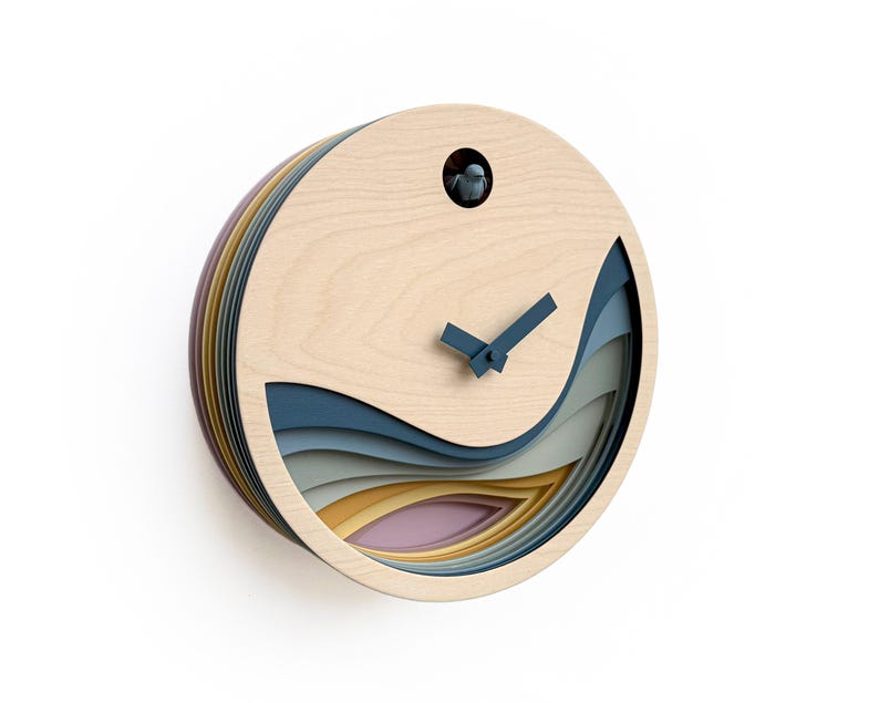 K&ouml;nnte beinhalten: Eine runde Holzkuckucksuhr mit einem geschichteten Design mit blauen, grauen, gelben und rosa Wellen. Die Uhr hat schwarze Zeiger und einen kleinen Vogel in der Mitte.