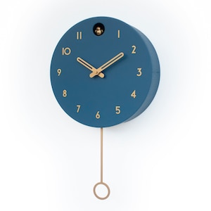May include: A blue round cuckoo clock with gold-colored hands and numbers. The clock has a pendulum with a gold-colored ring at the bottom.