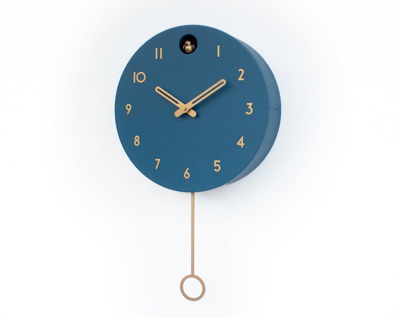 May include: A blue round cuckoo clock with gold-colored hands and numbers. The clock has a pendulum with a gold-colored ring at the bottom.
