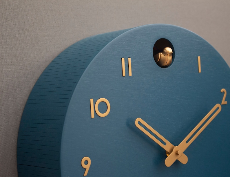 May include: A blue wooden cuckoo clock with gold hands and Roman numeral markings. The clock has a small bird cutout on the top.