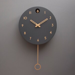May include: A black pendulum clock with gold Roman numeral hour markers and gold hands. The clock has a small bird cutout on the top.