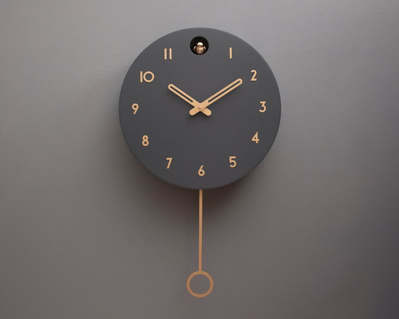May include: A black pendulum clock with gold Roman numeral hour markers and gold hands. The clock has a small bird cutout on the top.