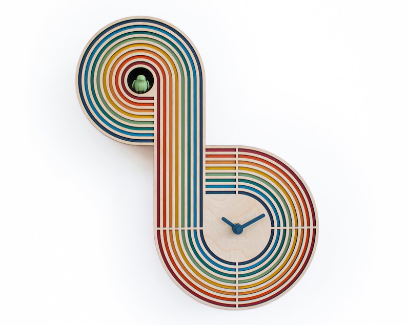 May include: A rainbow-colored wooden clock with a unique design. The clock face is in the center of the design, and the hands are blue. The clock is made of wood and has a rainbow-colored design.