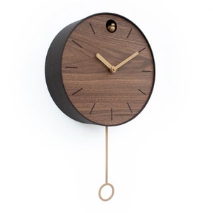 May include: A brown wooden cuckoo clock with gold hands and a pendulum. The clock has a round face with Roman numerals and a small bird that pops out of the top.