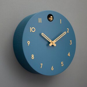 May include: A blue round clock with gold hands and gold numbers. The clock has a small bird cutout in the top.