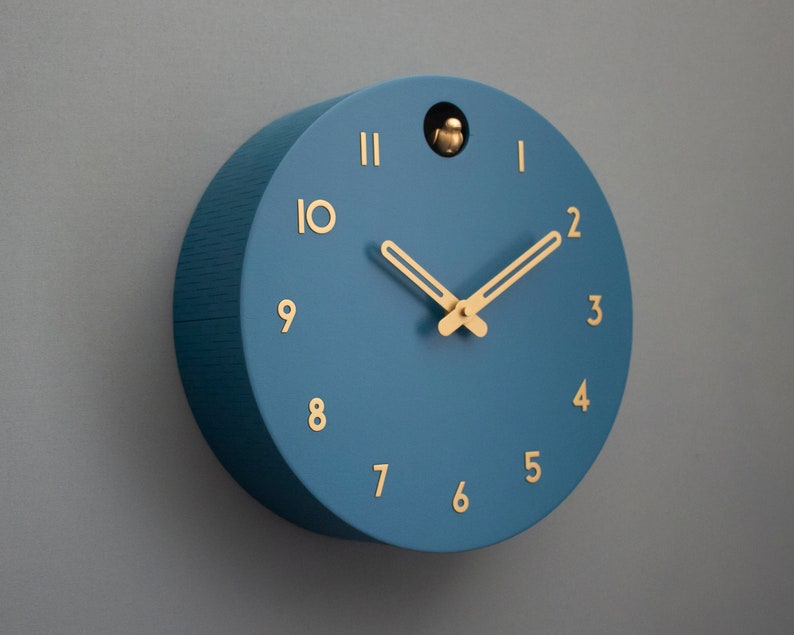 May include: A blue round clock with gold hands and gold numbers. The clock has a small bird cutout in the top.
