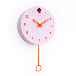May include: A round, light pink wall clock with orange numerals and hands. The clock has a small orange bird inside a hole at the top and an orange pendulum hanging below. The clock is mounted on a white wall.