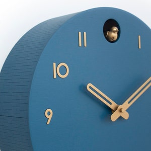 May include: A blue wooden cuckoo clock with gold hands and Roman numeral markings. The clock has a small bird that pops out of the top.