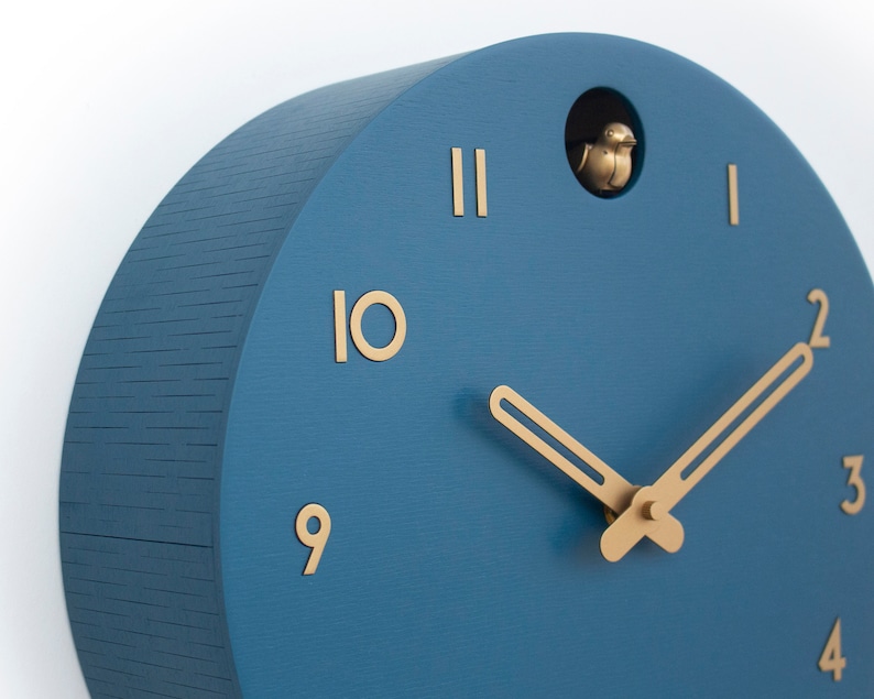 May include: A blue wooden cuckoo clock with gold hands and Roman numeral markings. The clock has a small bird that pops out of the top.