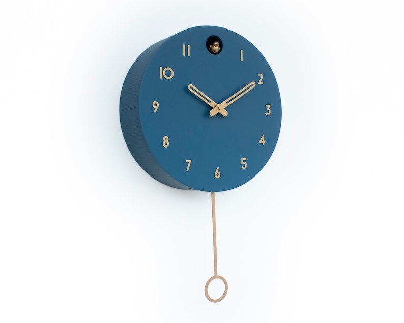 May include: A blue round cuckoo clock with gold-colored hands and numbers. The clock has a pendulum and a small bird cutout on the face.