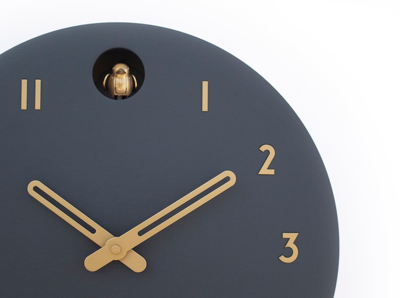 May include: A dark blue round clock face with gold hour markers and hands. The clock has a small opening at the top with a gold bird figurine inside.