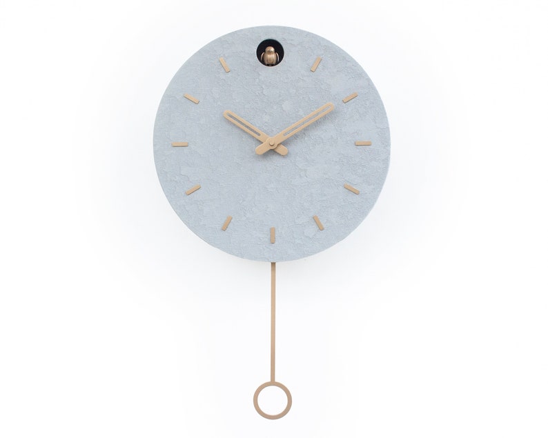 May include: A grey round cuckoo clock with gold hands and a gold pendulum. The clock has a textured surface and a small bird on the top.