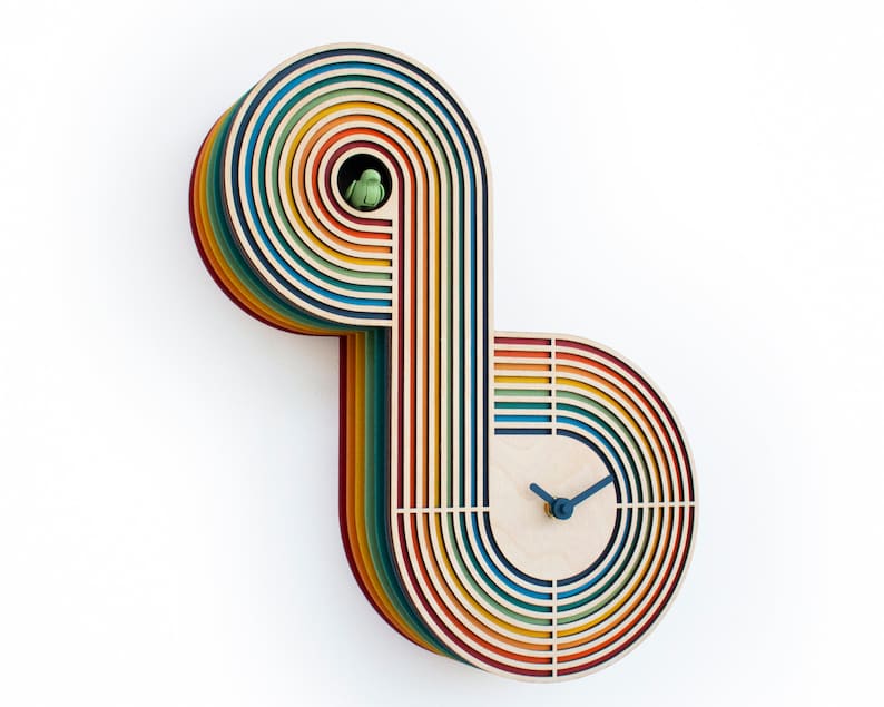 May include: A rainbow-colored wooden clock with a unique design. The clock face is circular and features a simple design with blue hands. The clock is made of layered wood strips, creating a colorful and eye-catching design.