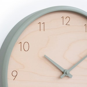Könnte beinhalten: Eine runde Uhr in Hellgrün mit einem hellen Holzgesicht und schwarzen Zahlen. Die Uhrzeiger sind ebenfalls hellgrün.