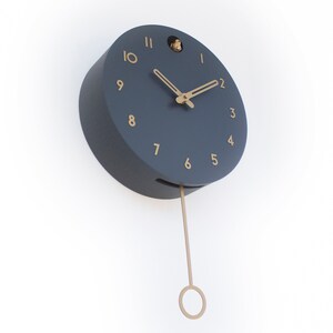 May include: A dark blue round clock with gold numbers and hands. The clock has a pendulum and a small bird cutout on the top.