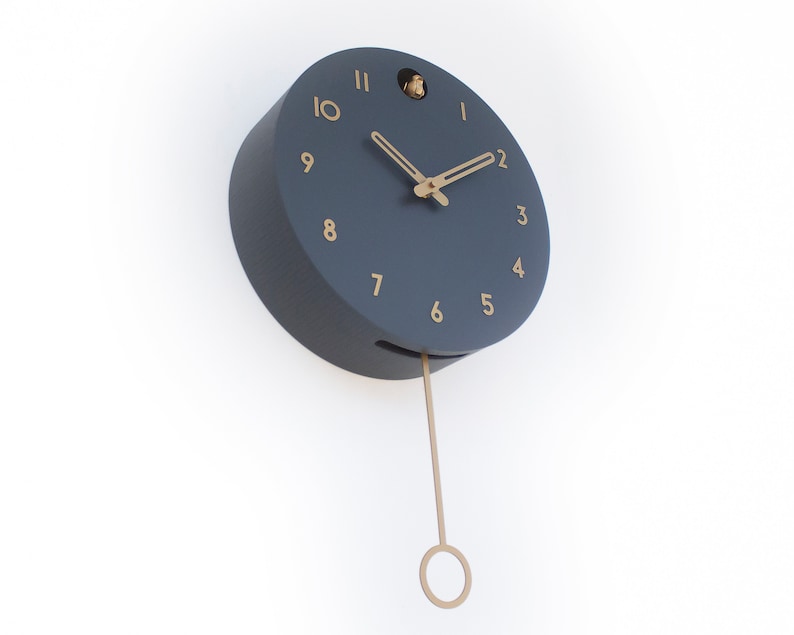 May include: A dark blue round clock with gold numbers and hands. The clock has a pendulum and a small bird cutout on the top.