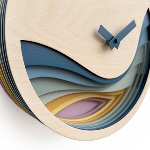 K&ouml;nnte beinhalten: Eine Wanduhr aus Holz mit einem geschichteten Design, das ein Wellenmuster in Blaut&ouml;nen, Gr&uuml;n, Gelb und Rosa aufweist. Die Uhrzeiger sind blau und das Zifferblatt der Uhr ist aus Naturholz.