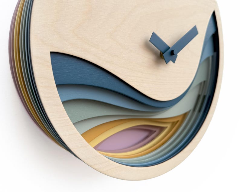 K&ouml;nnte beinhalten: Eine Wanduhr aus Holz mit einem geschichteten Design, das ein Wellenmuster in Blaut&ouml;nen, Gr&uuml;n, Gelb und Rosa aufweist. Die Uhrzeiger sind blau und das Zifferblatt der Uhr ist aus Naturholz.