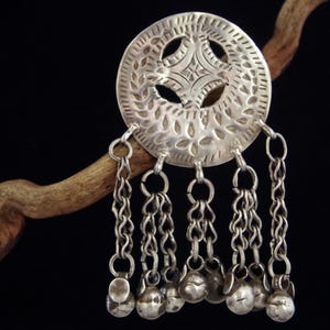 Puede incluir: Un colgante de plata con un diseño circular que presenta intrincados recortes y una cadena colgante con pequeñas bolas de plata.